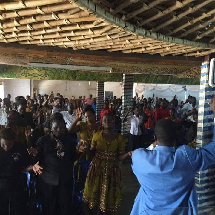 A crowded community worship gathering under a thatched roof